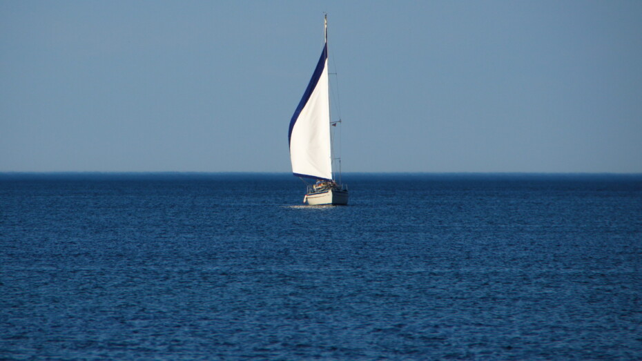 Segelschiff auf dem Meer Nur Wasser zu sehen und mittig das Segelboot. Weißes Segel mit blauem Rand