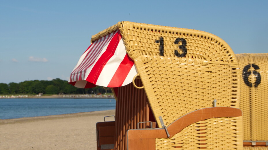 Strandkorb am Meer in der Sonne Nummer 13 drauf Rot Weißes Sonnendach Verschlossen 6 im Hintergrund und das Meer ist zu sehen